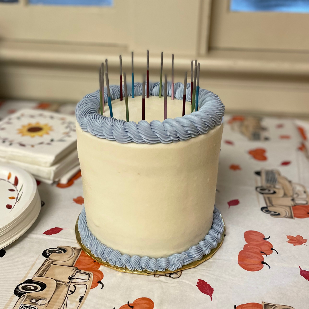 all white buttercream cake with blue frosting trim and tall thin birthday candles.