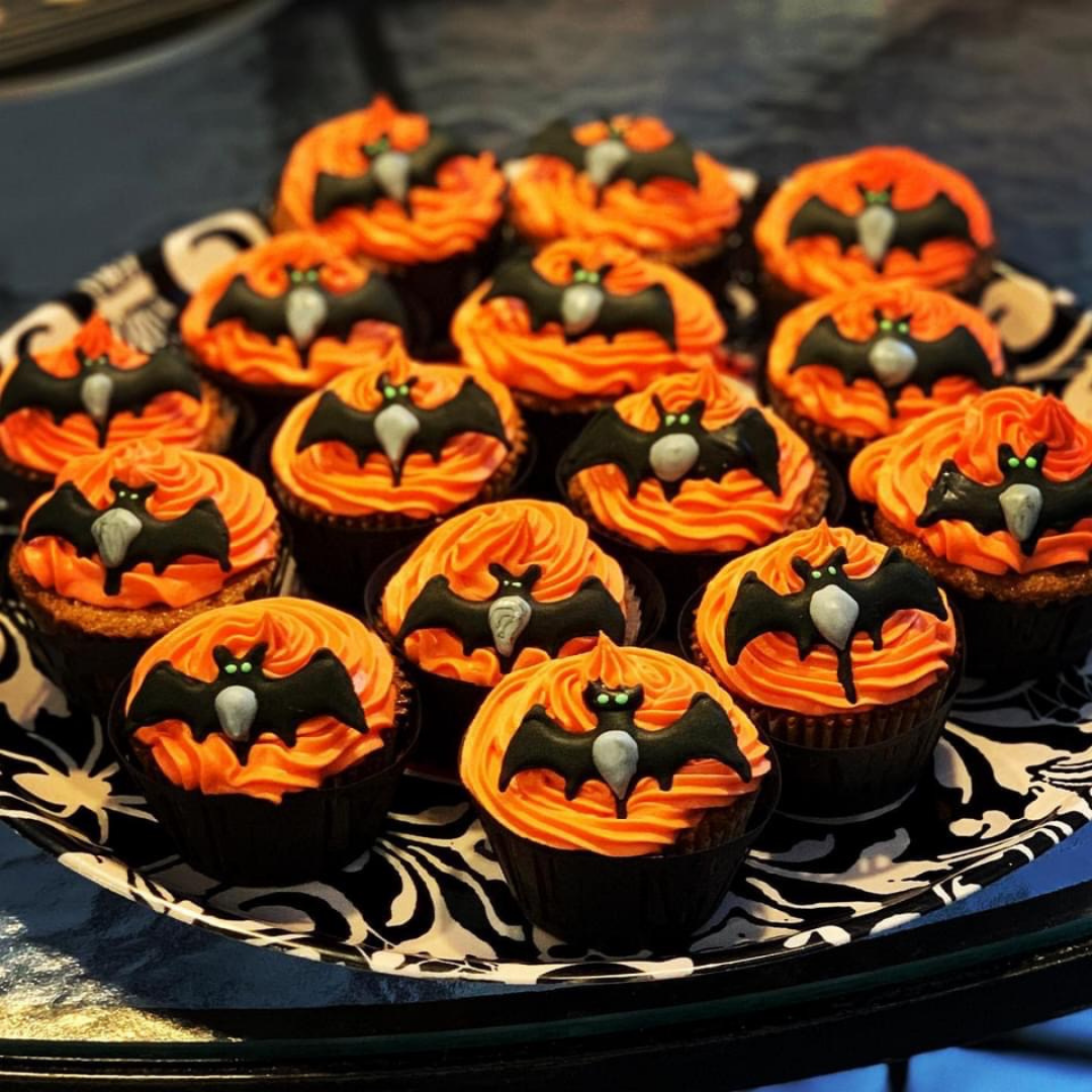 Chocolate cupcakes topped with orange swirled frosting and handmade royal icing black bats with glowing green eyes.