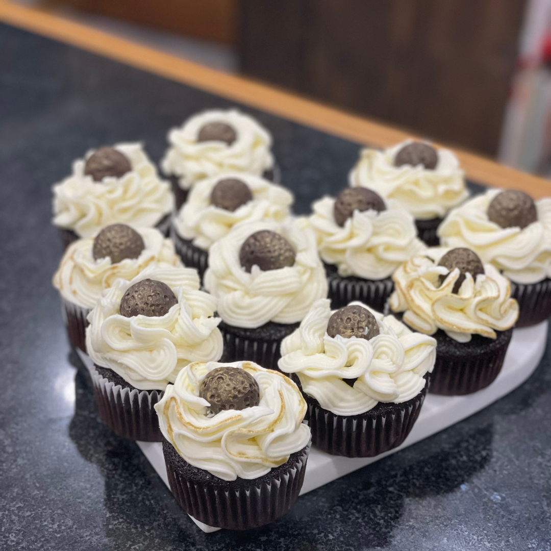 Chocolate cupcakes with swirled vanilla frosting and a handmade chocolate candy dusted with gold.
