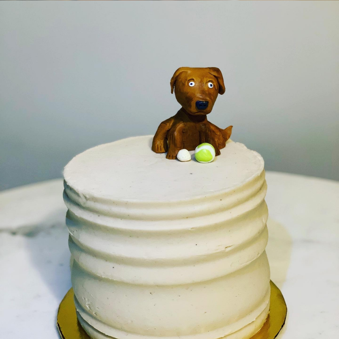 cake topped with a sculpted dog figurine and tennis ball.