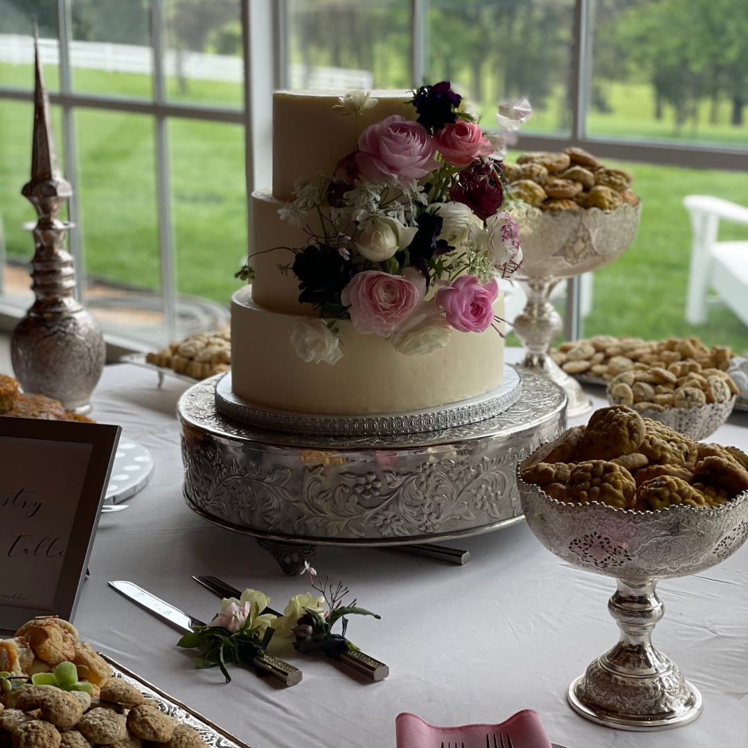 A three-tier white wedding cake decorated with pink and burgundy flowers on a silver stand.