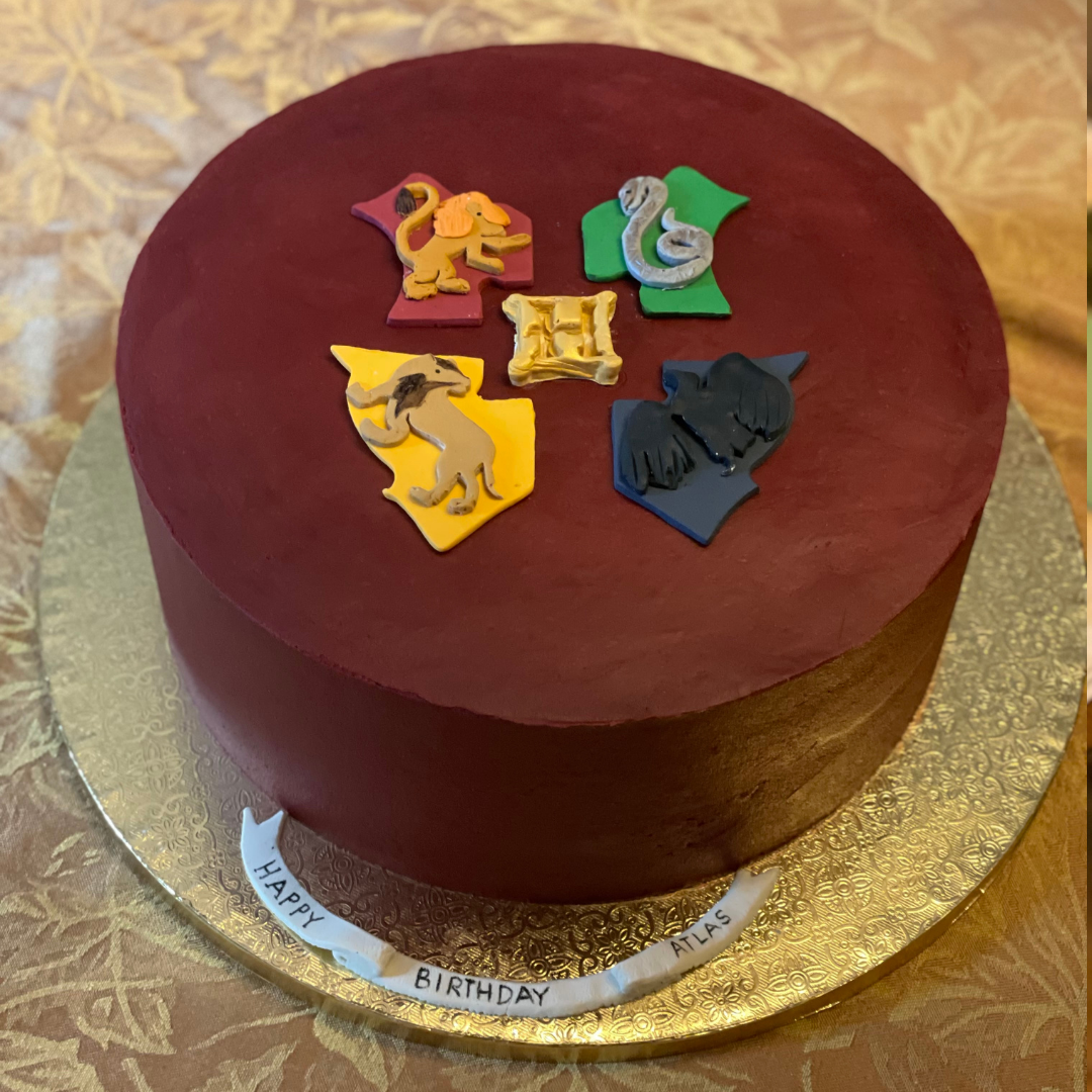 Burgundy Strawberry buttercream cake with Hogwarts house crest on top.