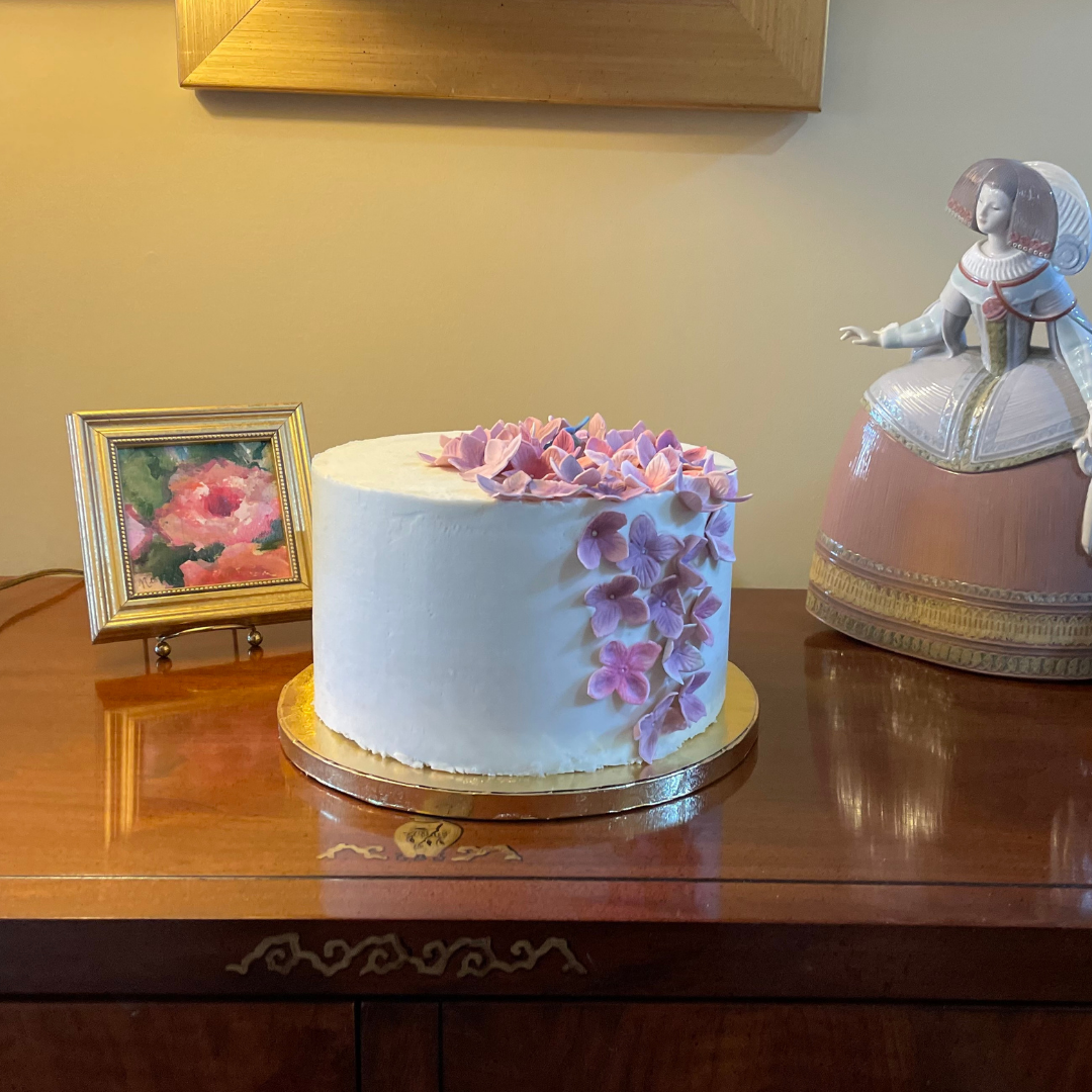 White buttercream cake decorated with cascading handmade pink and purple hydrangeas.