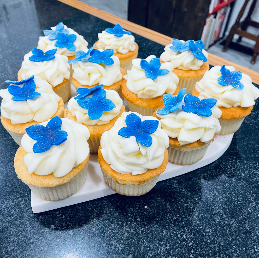 Vanilla cupcakes decorated with handmade sugar flowers resembling hydrangea petals.