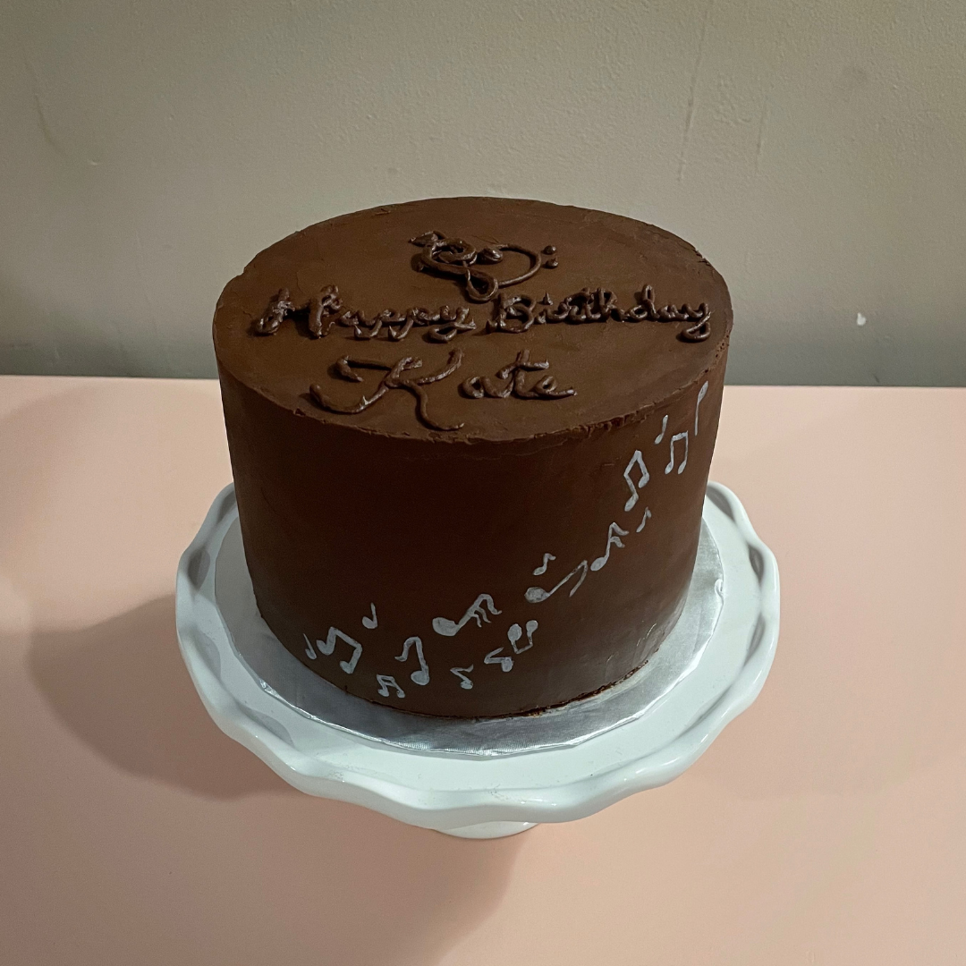Chocolate cake with silver musical notes and piped “Happy Birthday Kate” message.
