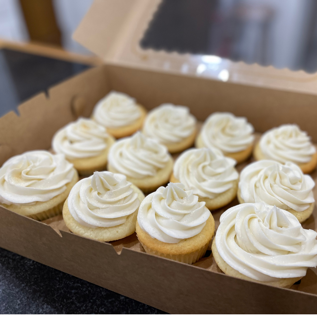 Simple vanilla cupcakes packaged in a bakery box with a clear lid, ready to go.