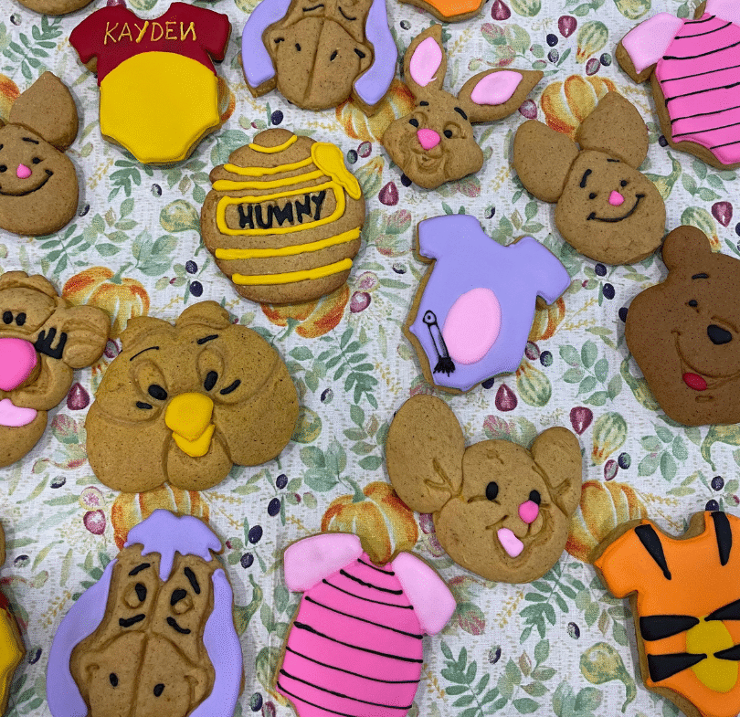 Royal icing cookies featuring Winnie the Pooh characters alongside character inspired onesie cookies.